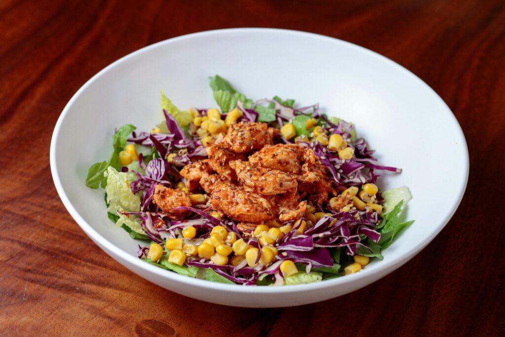 Delicious chicken salad bowl with fresh corn, red cabbage, and lettuce.