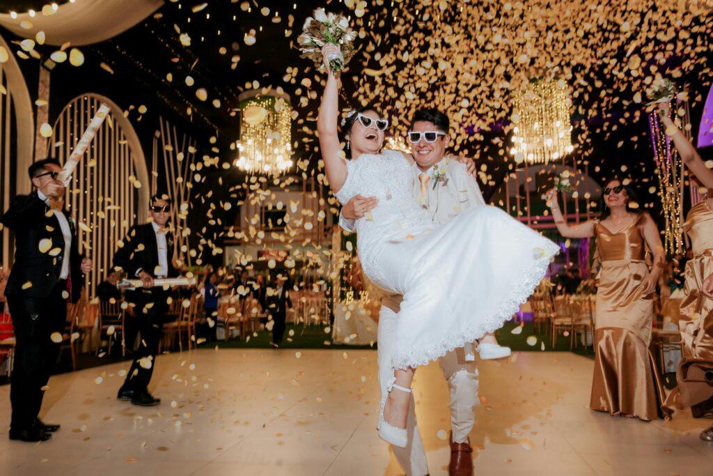 Bride and groom celebrate with confetti and friends in festive indoor wedding atmosphere.