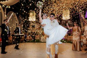 Bride and groom celebrate with confetti and friends in festive indoor wedding atmosphere.