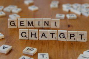 Close-up of wooden Scrabble tiles spelling Gemini and ChatGPT on a wooden surface.