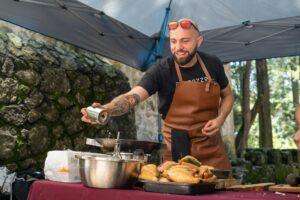 Bearded chef in apron seasoning food outdoors at a cooking event.