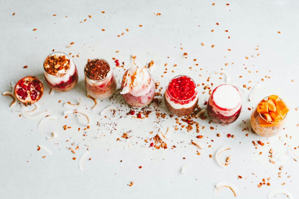 Colorful dessert glasses topped with fruits and nuts on a white table, captured in a delicious flat lay style.