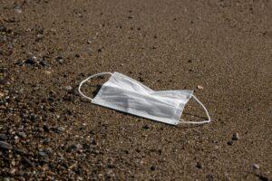A white face mask lies on a sandy beach, emphasizing pollution concerns and environmental impact.