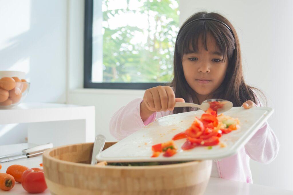 Child in kitchen preparing a fresh and healthy meal with vegetables.