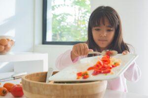 Child in kitchen preparing a fresh and healthy meal with vegetables.