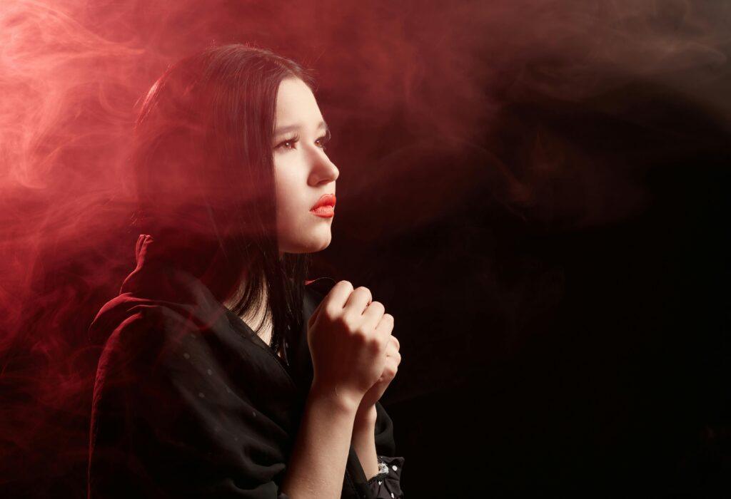 An artistic portrait of a woman praying in a smoky and moody environment.