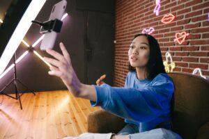 Asian woman creates live stream content in stylish neon lit room.