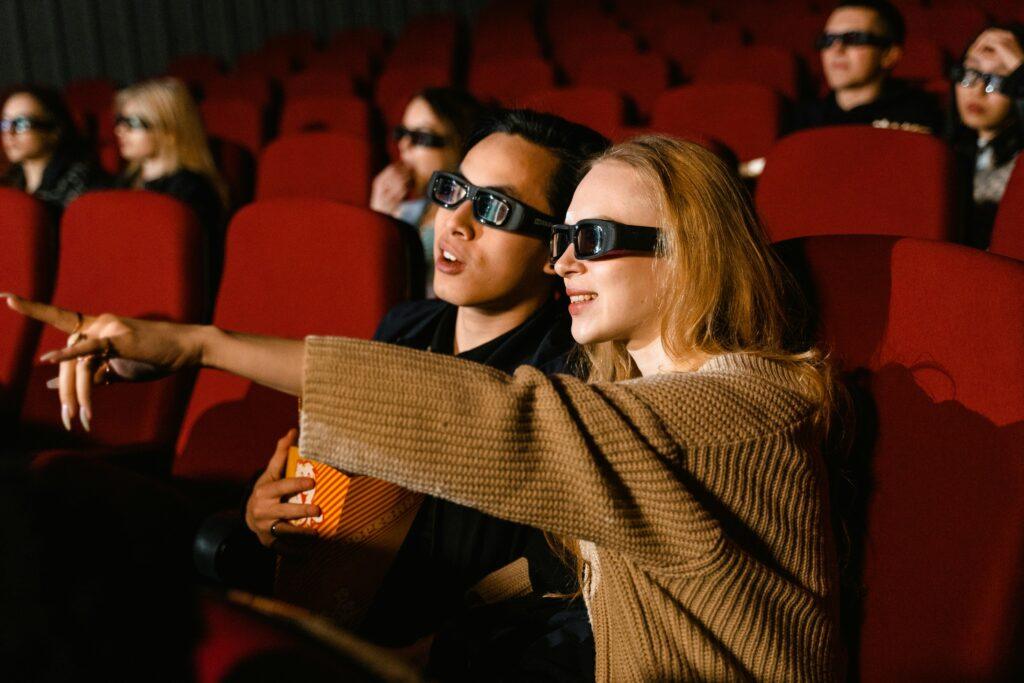 A couple wearing 3D glasses enjoy a movie at a theater, immersed in the experience.