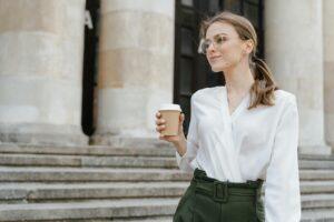 Elegant woman holding coffee cup, enjoying a casual day outdoors on stone steps.
